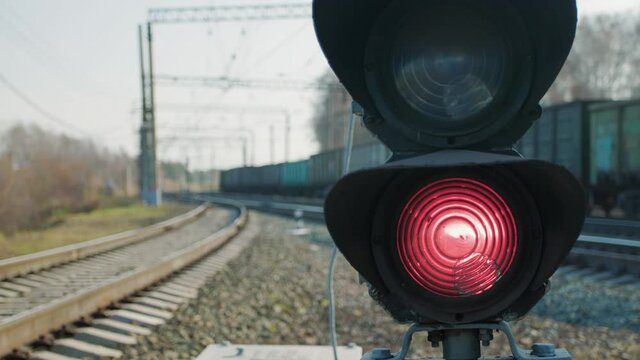The semaphore on the railway shines a red forbidding signal for trains. A heavy freight train is passing in the background. Sunny autumn day on the railway.