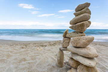 Zen stones stack balanced on beach with sea and clear blue sky in background