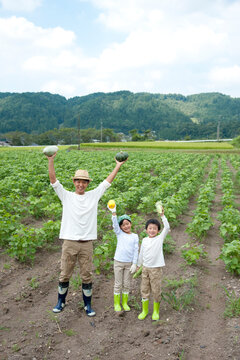 畑で収穫した野菜を持つ父と子供男女