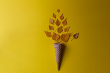 Yellow autumn leaves in a waffle cone on a yellow background. Autumn composition.
