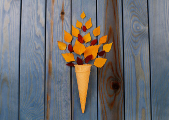 Yellow autumn leaves in a waffle cone on a blue wooden background Autumn composition.
