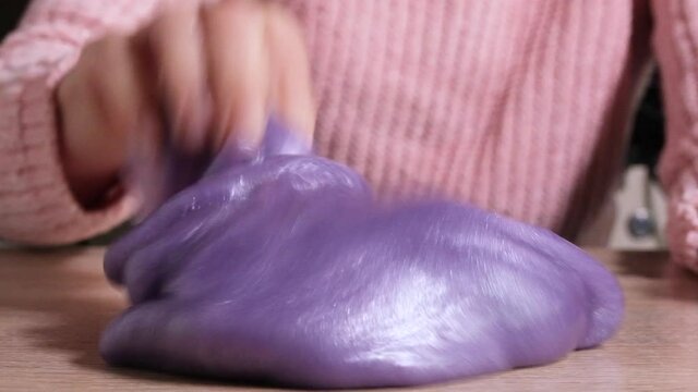 Playing with slime, stretching gooey substance for fun and stress relief. Close up and top view of female hand holding blue, pink and purple shining slime and squeezing it. Full HD slow motion video