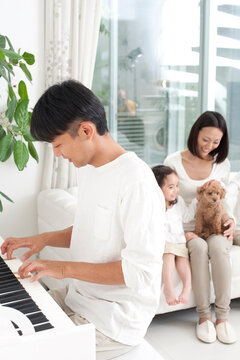 ピアノを弾く父とソファに座る母と女の子と犬