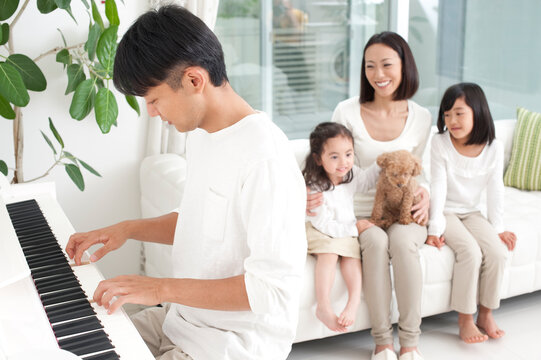 ピアノを弾く父とソファに座る母と子供男女と犬