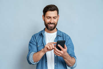 Smiling man using smartphone standing isolated on blue background copy space - obrazy, fototapety, plakaty