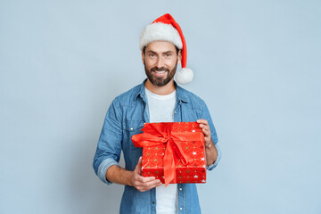 Portrait of smiling man in santa hat holding gift box over blue background