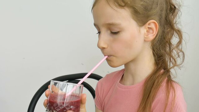 Sweet little girl drinks raspberry smoothie and smiles. Vegetarian drink. Close-up portrait of a child who enjoys a refreshing tasty raspberry juice, healthy eating