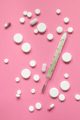 White medicines or pills and thermometer on a pink background. Weight loss products, vitamins, hormones or sedatives. Women's health concept.