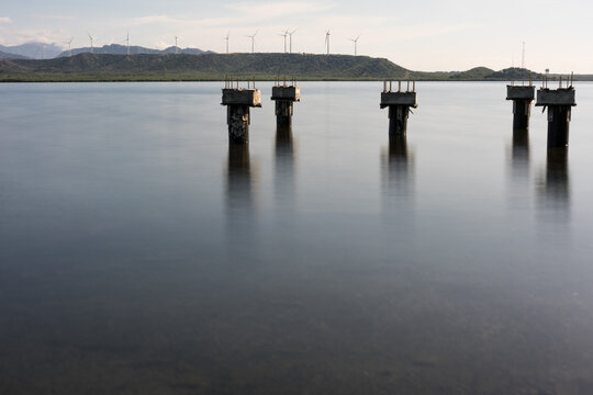 Dramatic long exposure image of piers in the Caribbean bay with wind turbines generating electricity in the background.