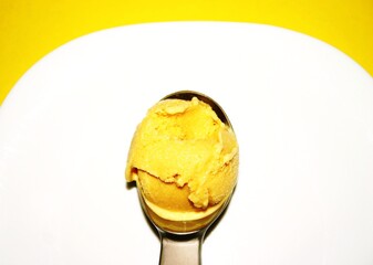 Mango ice cream. Ice cream scoop with mango ice cream on white plate. Yellow background.