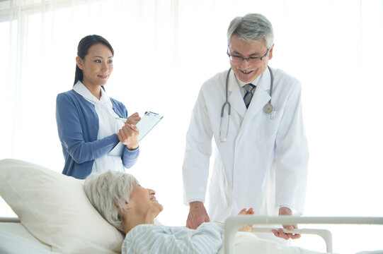 病院ベッドの老人を診察する医者と看護師
