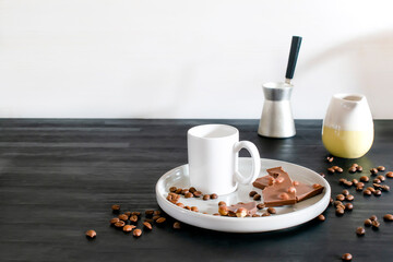 white espresso cup, mug, chocolate, coffee beans on plate kitchen table, utensils dishware, coffee pot on black wooden shelf. Early morning french home hot beverage breakfast, copy space