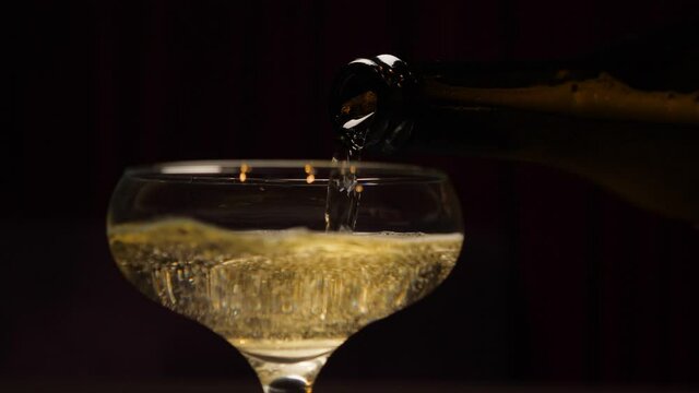 Bottle champagne slow pouring in glass closeup. Sparkling wine slow motion. Close up pour champagne in glass. Sparkling wine bottle pouring into glass. Celebration champagne new years eve party drink