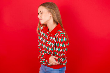 Young beautiful caucasian girl wearing christmas sweaters on red background got stomachache