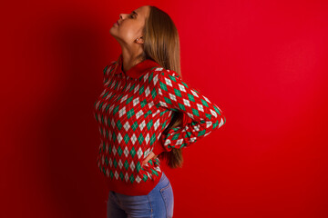Young beautiful caucasian girl wearing christmas sweaters on red background got back pain - obrazy, fototapety, plakaty