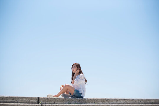 海の堤防に座ってスマホで音楽を聴く女性