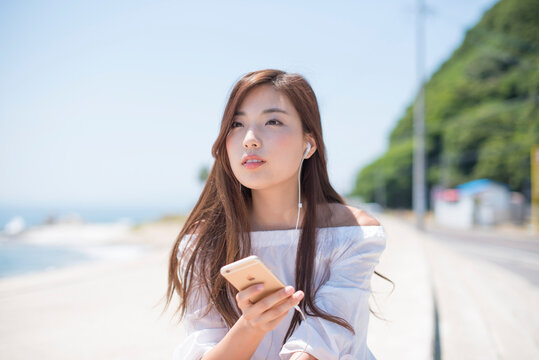 海の堤防に座ってスマホで音楽を聴く女性