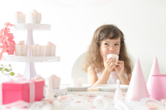 ピンクテーマのパーティでカップケーキを食べるハーフの女の子