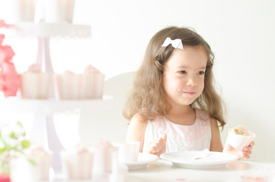 ピンクテーマのパーティでカップケーキを持つハーフの女の子