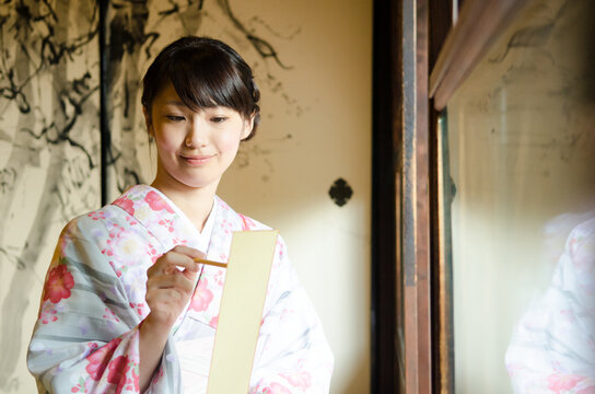 短冊に筆で俳句を書く着物姿の女性