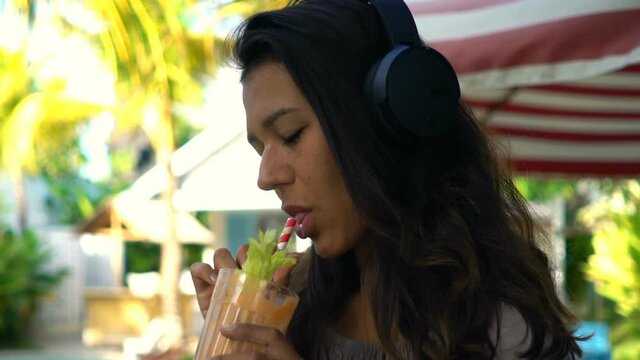 Young woman listening to music, drinking cocktail at garden cafe