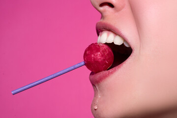 Closeup female lips with pink lipgloss holding in mouth red lollipop candy. Lollipop lips woman...