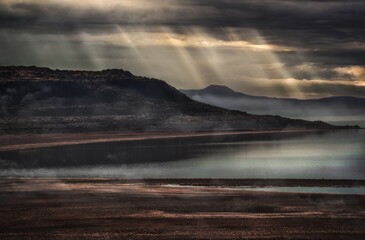 This image captures the beauty of an epic Utah landscape with a dramatic sky and sun beaming over a body of water.