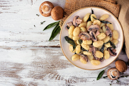 Gnocchi with mushrooms in a brown butter sage sauce. Above table scene on a rustic white wood background. Copy space.