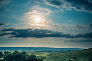 Field, sky and bright sun in the sky in the evening.