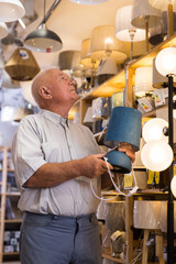 Portrait of mature man customer choosing table lamp at store of household goods