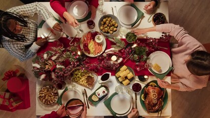 Friends celebrating new year, sitting at dining table top view. International young people eating delicious dishes, putting food on plates. Diverse students during christmas party at home. - Powered by Adobe