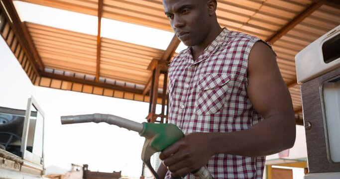 African american man in sleeveless shirt using fuel pump at petrol station