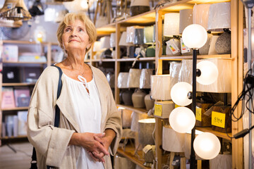 Mature female buyer choosing trendy lamp in modern furniture store