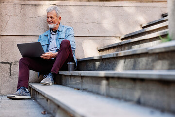 A senior student sits on the stairs of the university building and uses his laptop to look at notes before an exam.