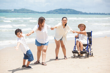 Disabled woman asia in a wheelchair with his family on the beach. Wheelchair woman sitting relax on...