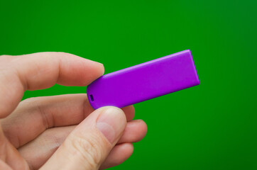 hand holds a purple flash drive for storing and transmitting data on a green background