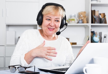 Happy mature woman in headphones with microphone communicating via internet