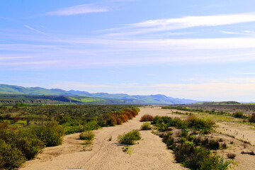 Fototapeta na wymiar dry riverbed sandy deserted desert land with mountains and hills under a blue cloudy sky