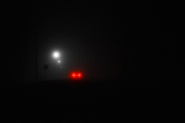 mystical dense fog on night street lit by lanterns, the red light of the car's brake light is...