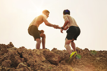 Silhouette of trail runner with hand helping each other hike up a mountain top together with sunset background. Help and support concept. - obrazy, fototapety, plakaty