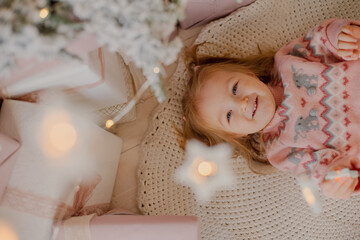 Portrait of a charming little girl lying under a Christmas tree. A New Year's gift. Christmas 2022.