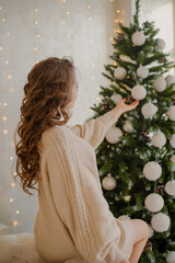 The theme of Christmas and New Year. A girl dresses up a Christmas tree for Christmas 2022.