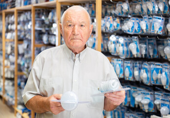 Mature man visiting store of household goods in search of energy efficient light bulbs