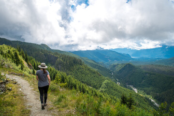 A woman walking on the hiking trail near Squamish BC, tall forested mountains, path towards the Watersprite Lake