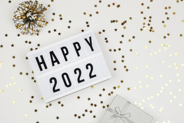  lightbox with words happy 2022, gift box and holiday confetti on white background. top view new year celebration.