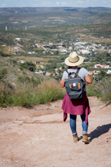 Fototapeta na wymiar Hispanic girl from behind with backpack and hat hiking adventure in a rugged landscape.