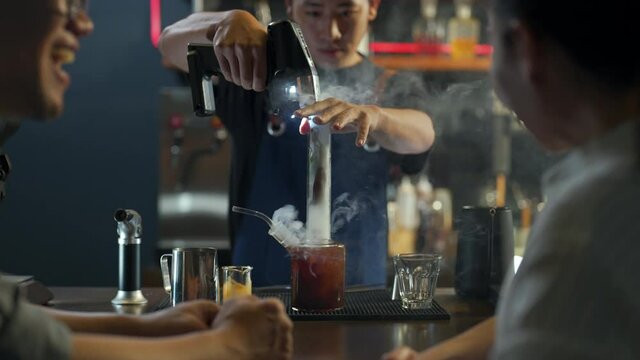 4K Asian man barista making signature coffee drink in special cocktail on bar counter to customer at coffee shop. Male coffee shop owner serving cold drink coffee to customer. Small business concept.