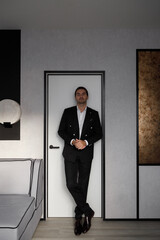 Fototapeta premium A gorgeous man in a suit in the room, preparing for the wedding. The groom is in black, in a stylish modern interior.