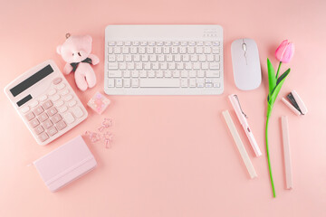 Top view of cute feminine soft pastel pink theme desktop workspace which consists of calculator, notebook, pens, mouse, keyboard, stapler, small teddy bear and a pink tulip. With copyspace.