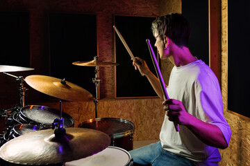 Drummer playing drums while sitting at drum kit with colorful backlit on background. Rock musician...